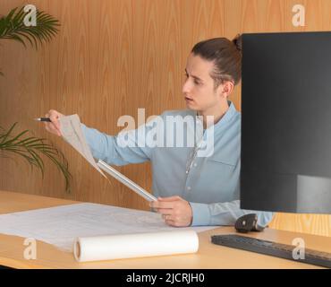 Young man focused looking at a sketch while designing an architecture project in front of the computer Stock Photo