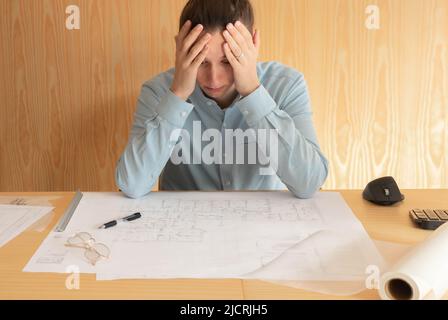 Stess, overwork and deadline. Tired unshaven young architect freelancer having headache while working in big architectural project at home office, fee Stock Photo