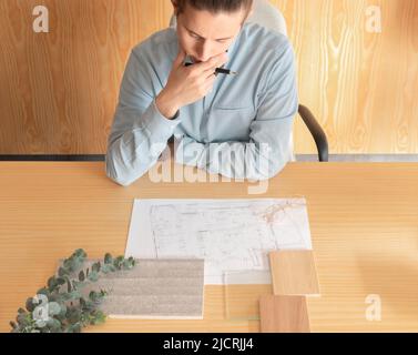 Top view of man thinging in new interior design project with material moodboard and samples on the table with floor plans Stock Photo
