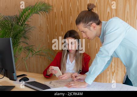 Two workers showing pictures on their smartphones as they chat about the project in the office Stock Photo