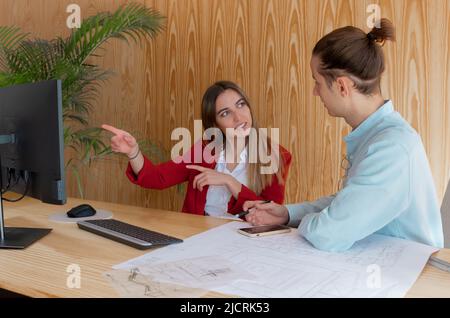 Man and woman chatting and pointing the computer screen showing new ideas with blueplints on the desk Stock Photo