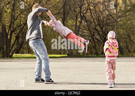 Dad plays with his daughters in the park. Twirling a girl around. Family. Stock Photo