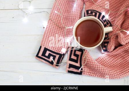 Cup of tea or coffee, knitted sweater and garland on a light wooden background Stock Photo
