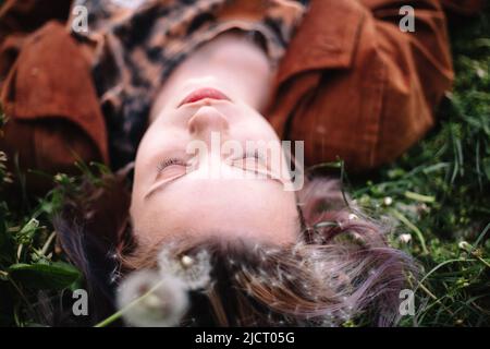 Close up portrait of peaceful teenage girl lying on grass in spring Stock Photo