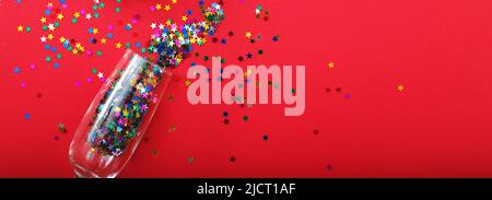 Champagne glass with star shaped sequins on a red background. Party, christmas, new year, celebration concept. banner. Top view. Flat lay. Stock Photo