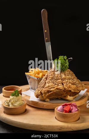 Pork knuckle Served with french fries and mashed potatoes on wooden cutting board Stock Photo
