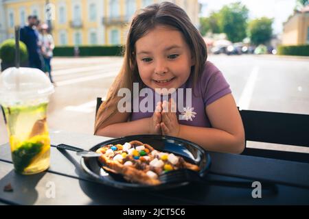 An 8 year old girl eats a Viennese waffle in a street cafe. High quality photo Stock Photo