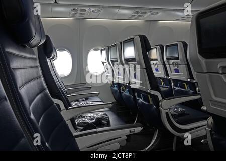 Empty rows of leather seats in the economy class section of a commercial airliner jet are shown in a horizontal view during the day. Stock Photo