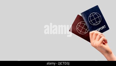 Banner with woman hand holding two passports. Multiple, dual nationality, change of citizenship, residency status. Copy space on grey background. High quality photo Stock Photo