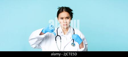 Upset asian woman shows thumbs down, dislike something, looking ...