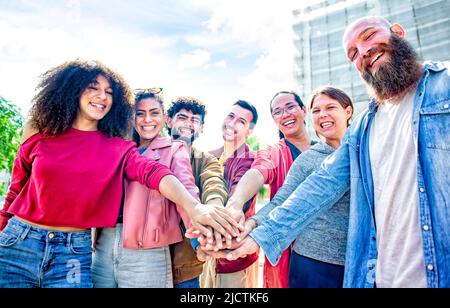 portrait of happy diverse large group of multicultural friends holding hands making high five stacking them together outdoor. convivial people Stock Photo