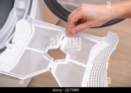 A man takes a lint filter out of the dryer and cleans it from dust, lint, hair, wool. Stock Photo