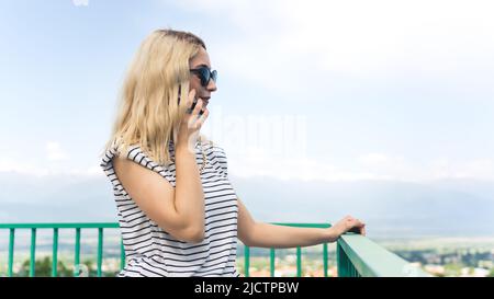 young blond girl talking on a phone in the park, medium shot outdoor. High quality photo Stock Photo