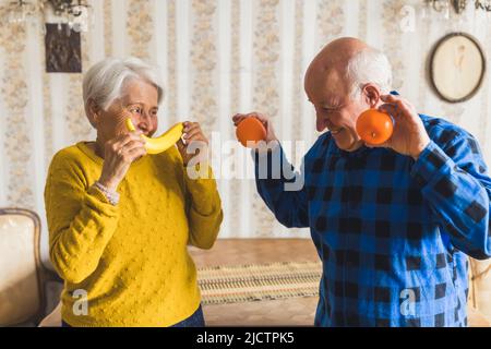 joyful senior Caucasian couple holding a banana and oranges medium shot indoor healthy eating concept. High quality photo Stock Photo