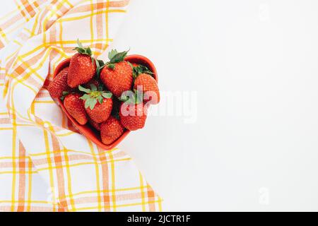 Fresh-picked strawberries in heart-shaped bowl on white background, concept of healthy eating vegan food. Summer snack. Closeup, selective focus, copy space Stock Photo