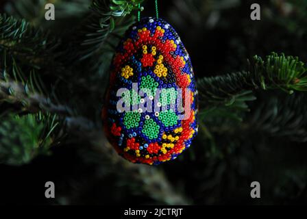 Christmas- Close up of a colorful homemade tree ornament made of egg shaped wax with a pattern of tiny multi colored beads pressed in. Stock Photo