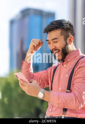 Asian businessman gesturing success while using to the mobile outdoors Stock Photo