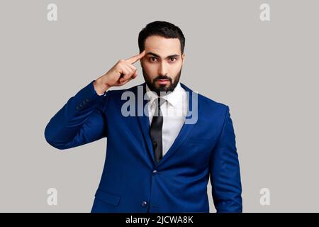 Unhappy frustrated bearded man showing stupid gesture, does not believe in his strengths, capabilities, disappointed, wearing official style suit. Indoor studio shot isolated on gray background. Stock Photo