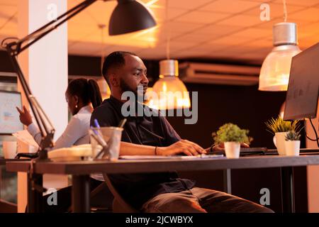 Confident male freelancer analyzing data charts on computer, doing research to create project report online on company network. Working with web information and sending email with documents. Stock Photo