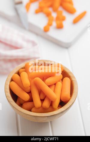 Baby carrot vegetable in bowl. Mini orange carrots on white table. Stock Photo