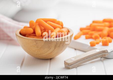 Baby carrot vegetable in bowl. Mini orange carrots on white table. Stock Photo