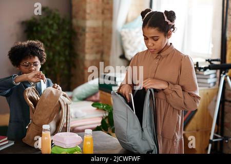 School children packing their books in school bags and lunch boxes while standing at table at home Stock Photo