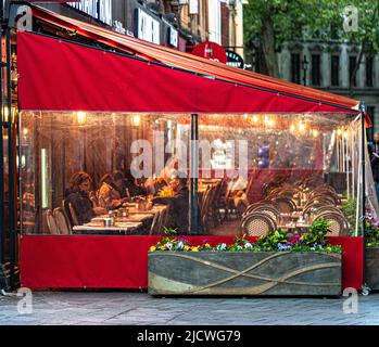 Restaurant customers seated at terrace under awning in rainy evening, London, England, UK. Stock Photo