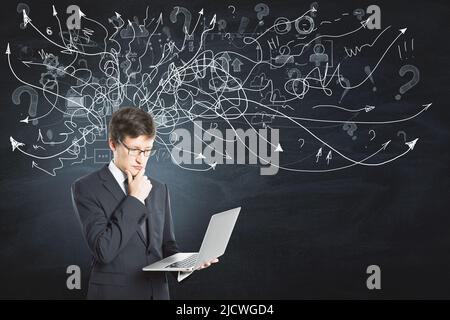 Find a solution and brainstorm concept with pensive businessman with laptop on dark background with hand drawn white chaotical arrows Stock Photo