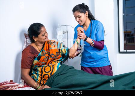 Nurse helping sick senior woman to stretch hand while doing routine exercise at home - concept of caregiver, physiotherapist and medical treatment Stock Photo