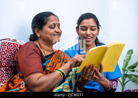 Nurse and sick women laughing by reading story from book at home - concept of relaxation, happiness and caring. Stock Photo