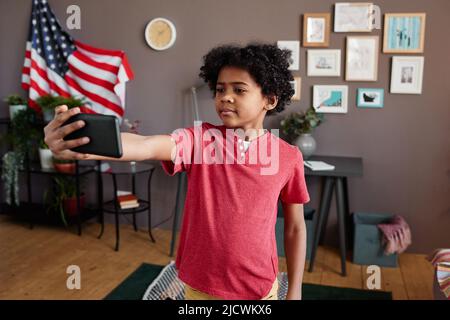 African little boy making selfie portrait on his mobile phone against his room Stock Photo