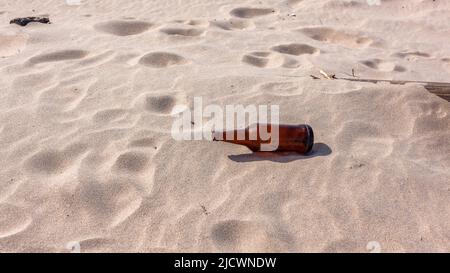 Beer alcohol bottle empty left on beach sand . Stock Photo