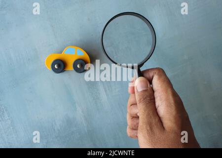 Hand holding magnifying glass and toy car. Car inspection, search, looking for car concept. Stock Photo