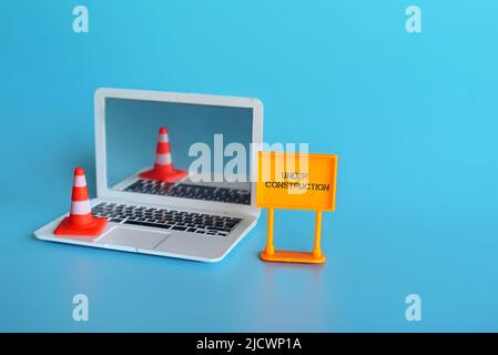Website under construction concept. Laptop, safety cone and signboard with text UNDER CONSTRUCTION. Stock Photo