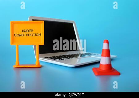 Website under construction concept. Laptop, safety cone and signboard with text UNDER CONSTRUCTION. Stock Photo