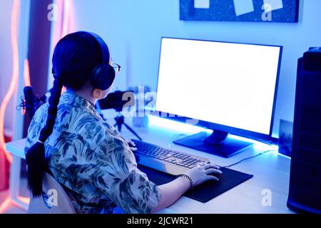 Portrait of teenage girl playing video games at night with computer screen mockup in blue neon lighting, copy space Stock Photo