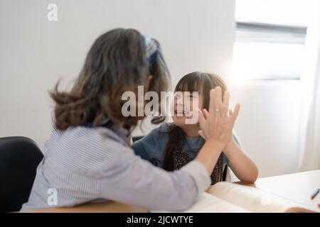 Little granddaughter and happy grandmother giving high five having fun playing together sitting on sofa, smiling grandma granny and preschool Stock Photo