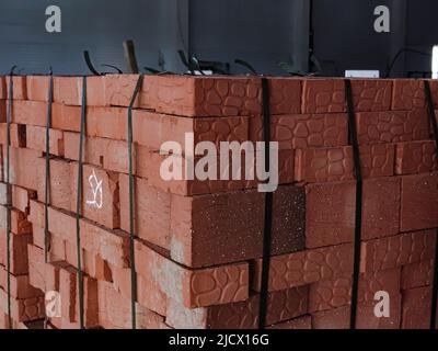 Red building bricks stacked on an outdoor warehouse. Material delivered from factory. Brick stored for building construction Stock Photo