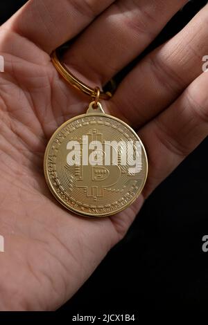 Bitcoin keychain in man hand on black background, close up. Stock Photo