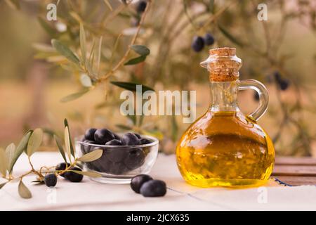 olive oil in a glass bottle and green olives on the background of olive branches in the garden Stock Photo