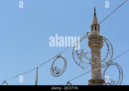 Ramadan decorations hanging in the street at Eid in front of a mosque minaret in Madaba in Jordan Stock Photo