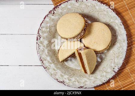 Classic Argentinean cornstarch and dulce de leche alfajores with coconut on a vintage plate. Top view. Copy text. Stock Photo