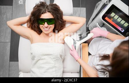 Top view of young smiling woman lying on sofa during laser hair removal procedure. Laser hair removal is pleasant, effective and painless method of unwanted hairless.