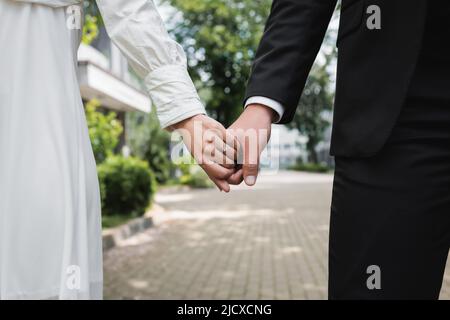 cropped view of bride in wedding ring holding hands with groom outdoors Stock Photo