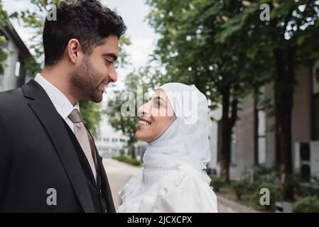 happy muslim bride in white hijab and groom in suit looking at each other Stock Photo