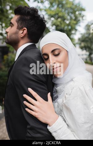 happy muslim bride in hijab and wedding dress hugging groom Stock Photo