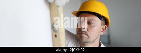 Man in helmet measuring wall using building level in apartment Stock Photo