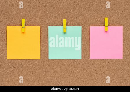Three multicolor sticky notes on cork bulletin board, reminder important information. Blank square paper, modern template, frame. Planning concept Stock Photo