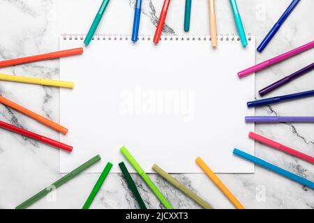 Background with pencils and white blank paper, felt pens frame. Open sketchbook. Mockup, template. Colored markers for drawing on a marble desk. Flat Stock Photo