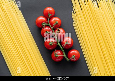 Top view of cherry tomatoes on branch between raw spaghetti on black background Stock Photo